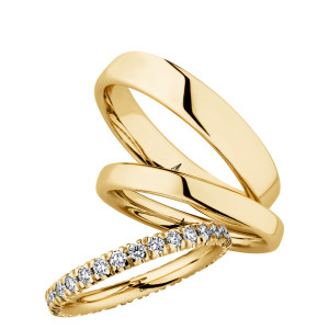 Christian Bauer 247100 18 karat yellow gold diamond wedding band, angled view of a rounded profile with round stones in shared prongs running around the full circumference, shown with its matching rings