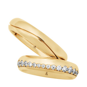 Christian Bauer 247143 18 karat yellow gold diamond wedding band, angled view of a polished dome with a continuous row of round stones set in a channel along one edge, shown with its matching ring