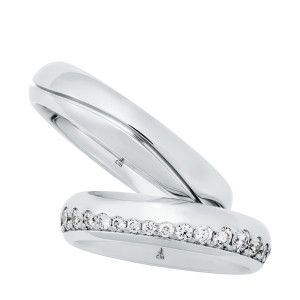 Christian Bauer 247143 platinum diamond wedding band, angled view of a polished dome with a continuous row of round stones set in a channel along one edge, shown with its matching ring