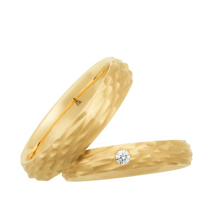 Christian Bauer 274788 18 karat yellow gold wedding band, angled view of a matte hammered surface of chisel cut facets covering the whole face and its irregular faceted edges, shown with its matching ring
