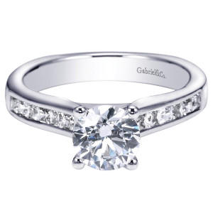Gabriel & Co. ER93965W44JJ 14 karat white gold Contemporary engagement ring, angled view of a round center in four prongs beside channel set square stones