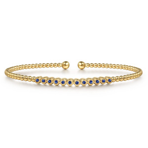 Gabriel & Co. BG4118-65Y4JSA 14 karat yellow gold Bujukan bangle, front view of a straight row of blue stones in rims with fine beaded edges, between ball ends