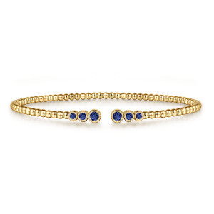 Gabriel & Co. BG4120-65Y4JSA 14 karat yellow gold Bujukan bangle, front view of the beaded cuff with blue bezel stones growing larger toward the gap on each side