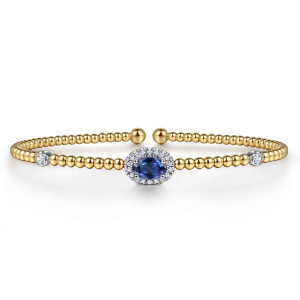 Gabriel & Co. BG4435-57M45SA 14 karat white and yellow gold Bujukan bangle, front view of the blue oval stone in its diamond halo with a small diamond on each side