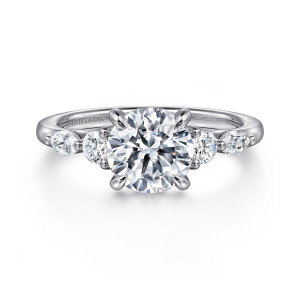 Gabriel & Co. ER16199R6W44JJ 14 karat white gold Contemporary engagement ring, front view of the round center flanked by round and elongated diamonds on the shoulders