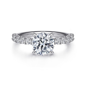 Gabriel & Co. ER16372R6W44JJ 14 karat white gold Contemporary engagement ring, front view of a round center flanked by a line of shared prong diamonds on the shoulders
