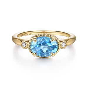 Gabriel & Co. LR51435Y45BT 14 karat yellow gold Hampton ring, front view of the sideways blue oval in a rope collar between milgrain bezel diamonds