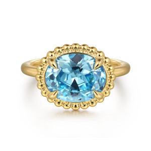 Gabriel & Co. LR52557Y4JBT 14 karat yellow gold Bujukan ring, front view of the blue oval stone lying sideways in four prongs inside its beaded rim