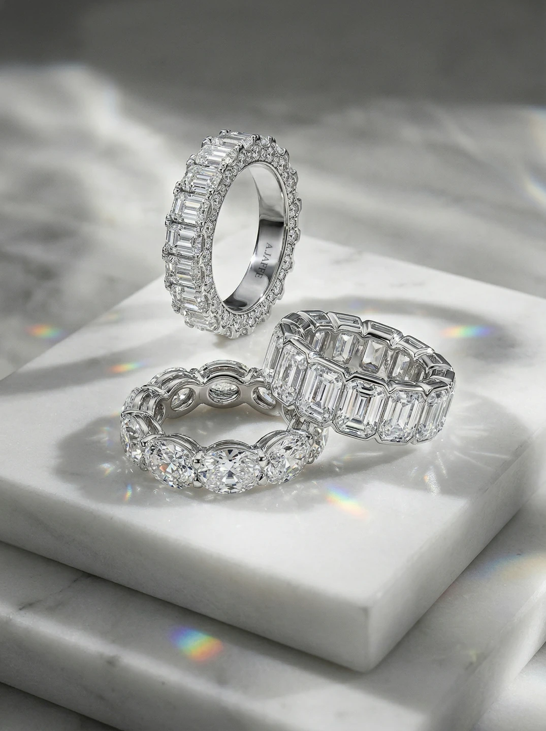 A.JAFFE emerald-cut and round diamond wedding bands arranged on pale stone